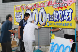 大幅な引上げを求めて模倣1円玉シールを「1000円横断幕」に貼付する府民
